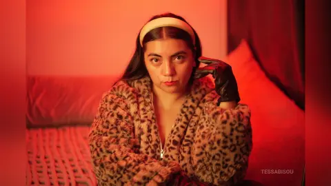 Woman in leopard print faux fur coat and black gloves sitting on a couch in warm red lighting.