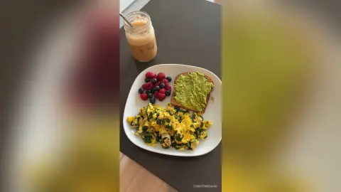 ChristineDavis's breakfast plate featuring scrambled eggs with greens, avocado toast, and a mix of red and blue berries next to an iced coffee.