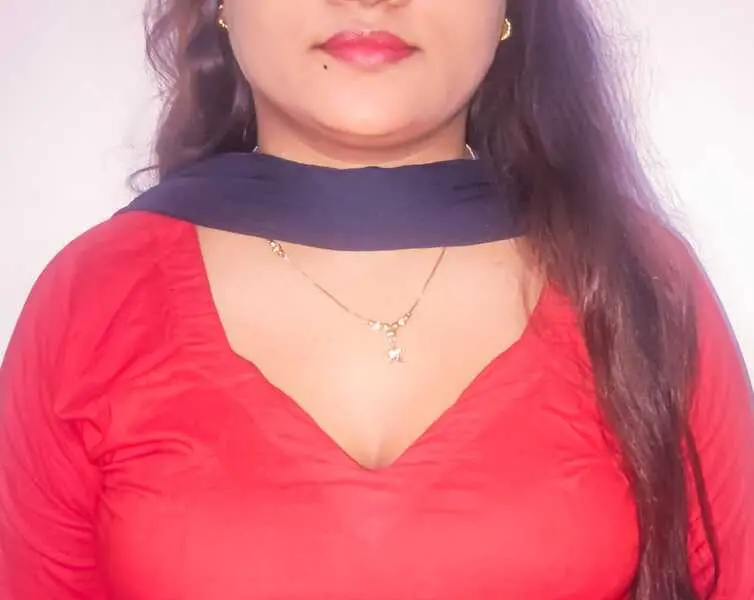 FairyBeauty1999 wears a red embroidered sari and a heavy, colorful jeweled necklace with red, green, and gold stones, showing her neck and shoulders.