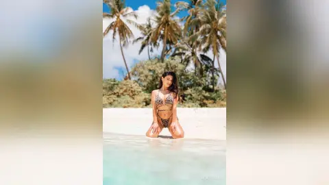 Woman in leopard print bikini relaxing on a tropical white sand beach under palm trees.