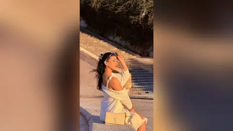 Stylish woman in a white summer dress sitting on stone stairs during a warm golden hour sunset.