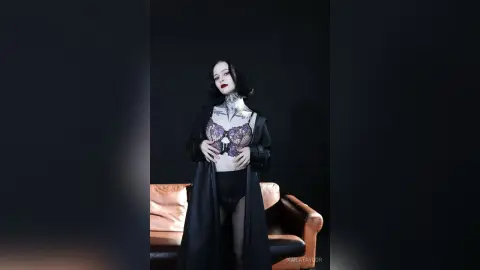 KailaTaylor poses in black lace lingerie and a long black robe, showing off her neck tattoos and dark hair while sitting on a brown leather sofa.
