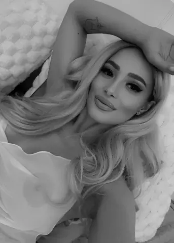 Blonde woman in white loungewear relaxing on a textured bed in a serene, moody black and white portrait.