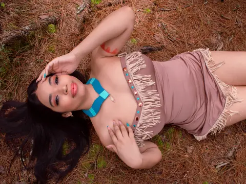 Woman in a dusty rose fringe bodysuit lying on pine needles in a forest setting with a dreamy mood.