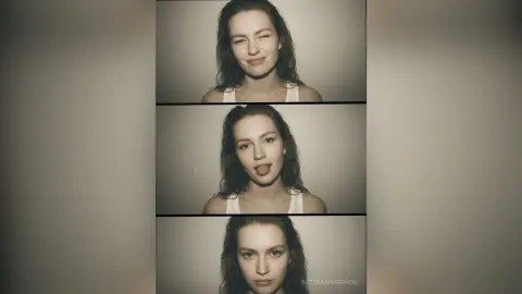 Playful woman in a white tank top winking and sticking her tongue out in a moody studio portrait.