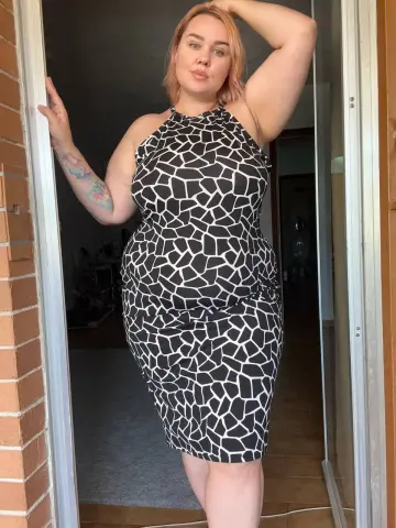 Curvy woman in a black and white geometric print halter dress standing in a doorway with a confident mood.