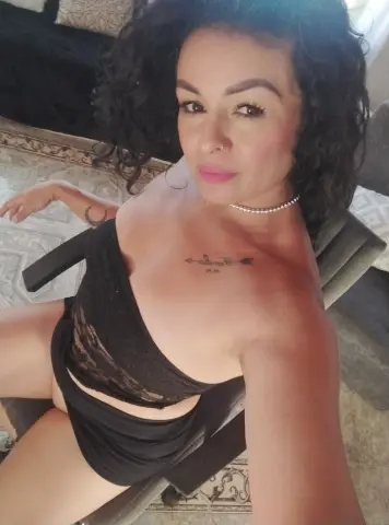 Woman with curly hair in a black lace outfit relaxing on a chair in a bright room.