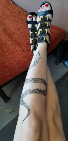 Woman with a large snake leg tattoo wearing black strappy sandals while relaxing on a red outdoor lounge chair.