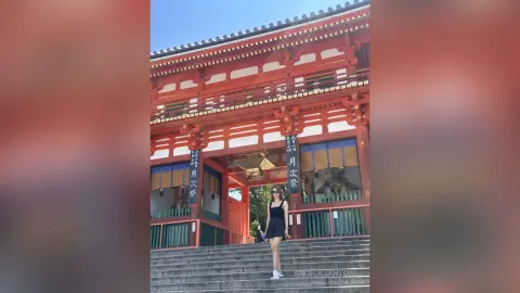 Young woman in a black dress standing before the grand red Senso-ji Temple gate in Tokyo, Japan.