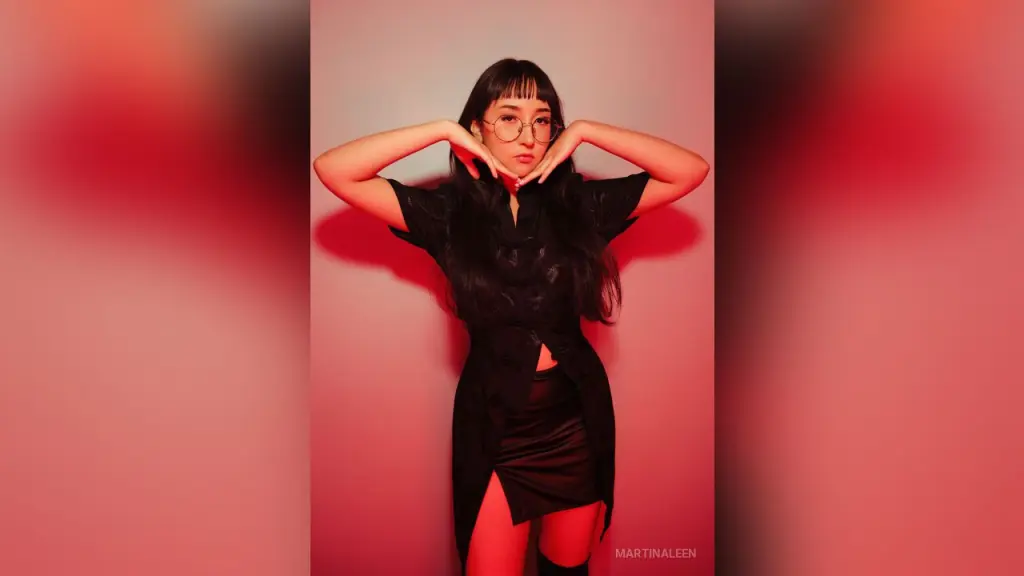 MartinaLeen β Stylish woman in a black button-down shirt and skirt posing against a moody red background.