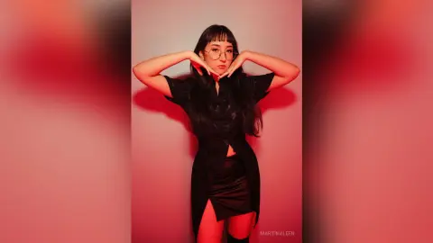 Stylish woman in a black button-down shirt and skirt posing against a moody red background.