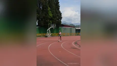 Athletic woman in blue sportswear training on a red running track under a cloudy sky.