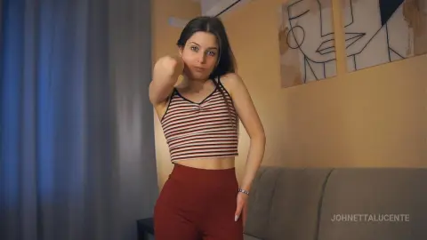Young woman in a striped tank top and red leggings posing in a cozy, sunlit living room.