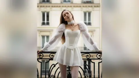 Elegant woman in a white puff-sleeve mini dress posing on a Parisian balcony with a dreamy mood.