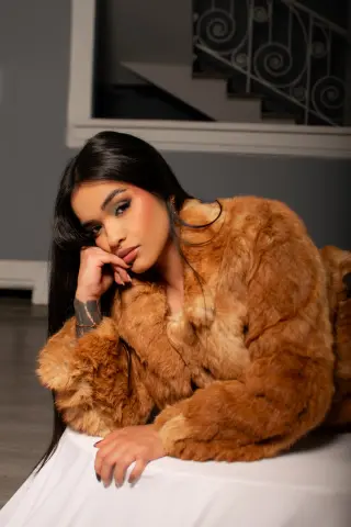 Glamorous woman in a cozy brown faux fur coat posing elegantly in a modern indoor setting.