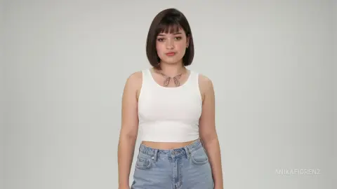 Young woman with short dark hair wearing a white tank top and blue jeans in a minimalist studio setting.