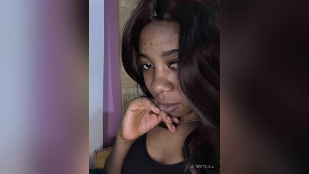 AlbertNina — AlbertNina poses with her hand under her chin, wearing a black tank top.