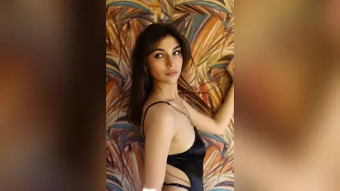 Elegant woman in a black satin bodysuit posing against a tropical leaf pattern background.