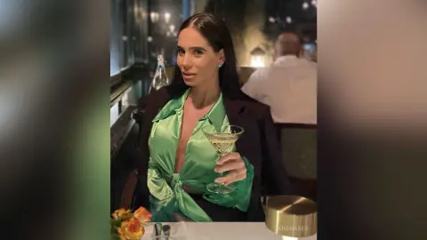 Elegant woman in a green satin blouse holding a cocktail at a sophisticated evening dinner setting.