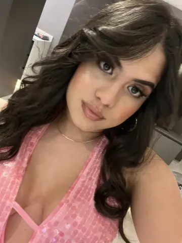 Leialeen — Young woman with long wavy hair wearing a pink sequin halter top in a modern indoor setting.