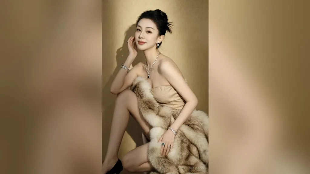 Elegant woman with dark hair in a bun wearing a red lace dress and flower earrings in a cozy living room.