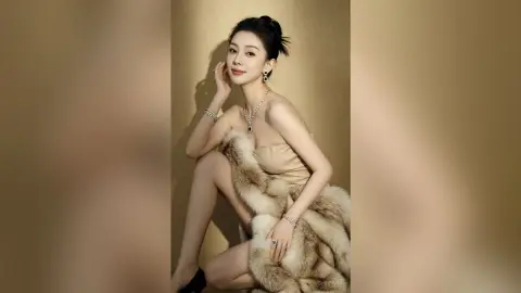 Elegant woman in a beige strapless dress and fur wrap posing gracefully against a neutral studio background.