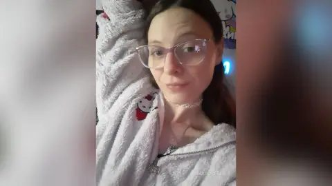 Young woman with glasses wearing a cozy white Hello Kitty fleece hoodie in a relaxed indoor setting.