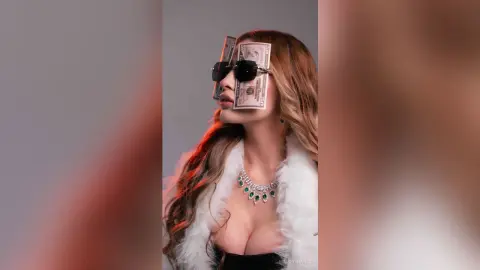 Glamorous woman in white faux fur and emerald necklace wearing sunglasses with dollar bills over her eyes.