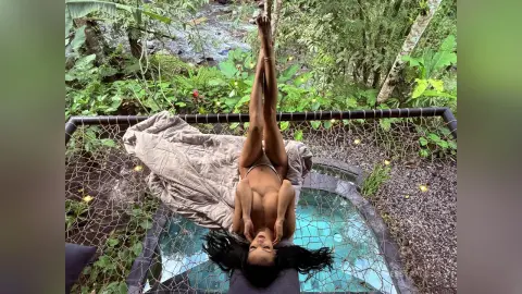 Relaxed woman in a bikini lounging on a jungle hammock net over a tropical river stream.