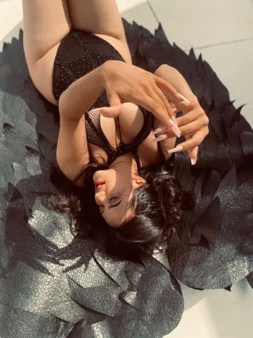 Woman in black lace bodysuit lying on large dark feathered wings in bright sunlight.