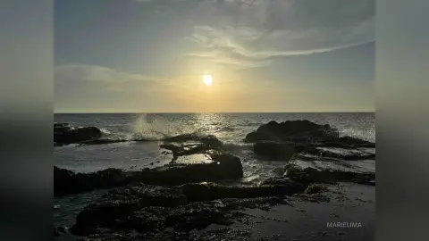Golden sunset over dark rocky tide pools on a serene coastal beach at dusk.
