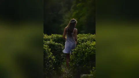 Dreamy woman in a white sundress walking through a lush green garden at twilight.