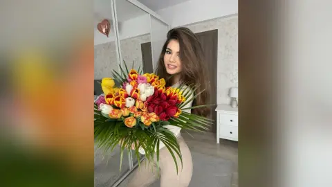 Smiling young woman in a white top holding a colorful bouquet of tulips in a bright modern room.