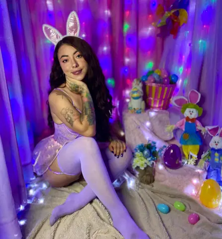 Smiling woman in lavender bunny costume and tights sitting in a dreamy purple Easter themed setting.