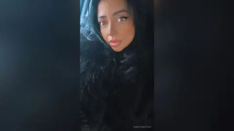Glamorous woman with long dark hair wearing a luxurious black faux fur coat in a moody, elegant setting.