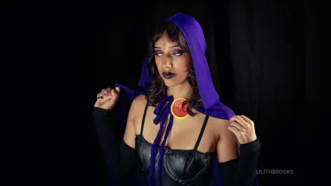 LilithBrooks wears a purple hooded cape and black leather bustier, posing against a dark background.
