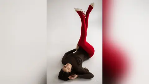 Fashionable woman in a black long-sleeve top and red leggings lying on a white studio background.