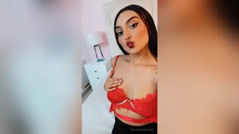 Young woman in red lace lingerie making a kissy face in a bright bedroom setting.