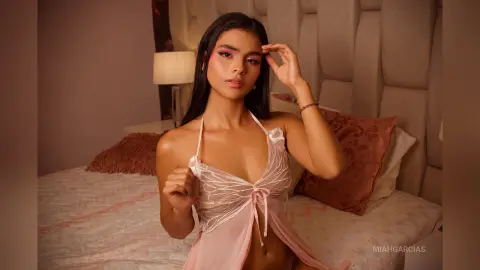 Young woman in a pink satin camisole relaxing on a bed in a cozy, warm-lit bedroom.