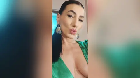 Glamorous woman in a green satin dress and large teardrop earrings posing with a confident expression indoors.
