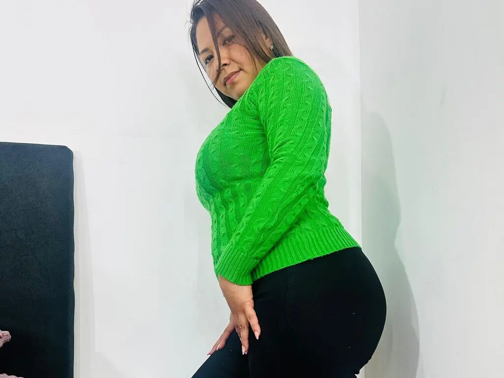Smiling woman in a bright green cable knit sweater and black leggings posing in a minimalist white room.