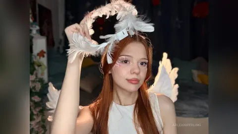 Redheaded woman in white angel costume with feathered wings and halo in a cozy indoor setting.