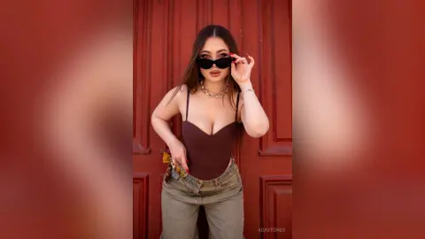 Stylish woman in a brown bodysuit and sunglasses posing confidently against a red door background.