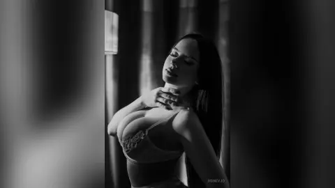 Moody black and white portrait of a woman in lace lingerie posing gracefully in soft indoor lighting.