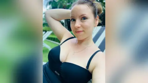 Smiling blonde woman in a black summer dress relaxing outdoors in a sunny garden setting.