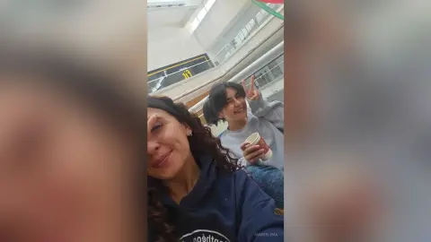 Two smiling young women in casual sweatshirts sharing a happy moment indoors with coffee.