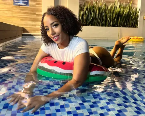 Smiling woman in white t-shirt relaxing on a watermelon float in a blue tiled swimming pool.