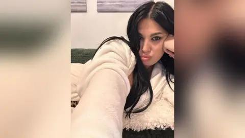 Young woman with long dark hair wearing a cozy white robe relaxing in a comfortable indoor setting.