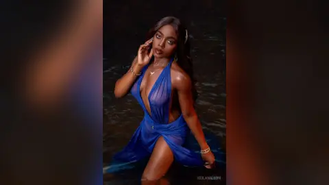 Glamorous woman in a blue plunging maxi dress posing in a dark water setting with a moody, elegant vibe.