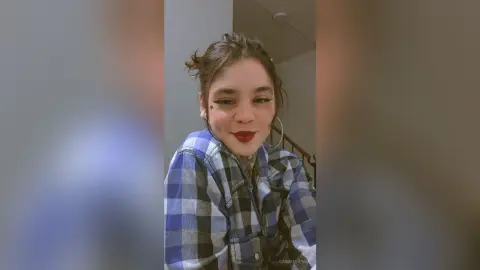 Smiling young woman in a blue plaid flannel shirt posing indoors with a casual, relaxed mood.